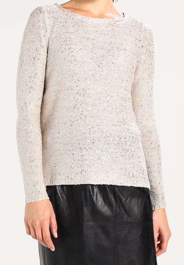 Suéter de punto de color beige claro con mangas largas, material texturizado y sutiles toques de brillo, combinado con una falda de cuero negra.