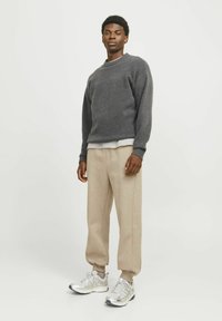Grå striktrøje med runder hals, beige sweatpants med elastiske manchetter og sølvfarvede træningssko med mesh-detaljer. Enkel og afslappet pasform.