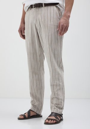 Helle beige gestreifte Hose aus weichem Stoff, mit geraden Beinen und lockerer Passform, kombiniert mit dunkelbraunen Sandalen mit mehreren Riemen.