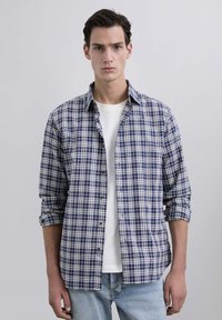 Camisa de cuadros en azul marino y blanco, de manga larga, con un corte relajado y cuello clásico, llevada sobre una camiseta blanca.