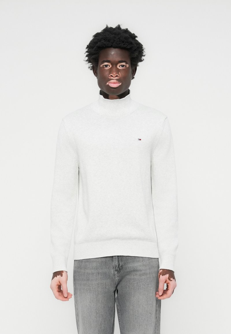 Lysegrå turtleneck genser laget av myk strikket stoff. Har ribbestrikkede mansjetter og nederkant. Lite logo på venstre bryst. Sammen med grå jeans.