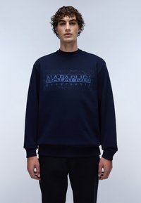 Sweatshirt bleu marine avec un imprimé graphique texturé affichant "NAPAPIJRI geographic" sur le devant. Manches et ourlet côtelés. Coupe décontractée.