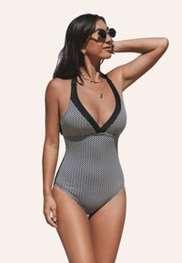 Maillot de bain une pièce à motif noir et blanc avec un décolleté en V profond et des bretelles contrastantes, présentant une silhouette ajustée et un tissu texturé.