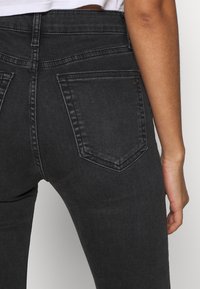 Svart denimjeans med hög midja, utrustade med två bakfickor och synlig sömnad. Tyget har ett slätt, något strukturerat utseende.