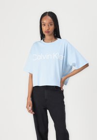 Ljusblå kortärmad croppad t-shirt med en vit "Calvin Klein" logotyp på framsidan, ihop med svarta högmidjade byxor.