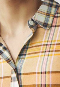 Camicia con bottoni caratterizzata da un pattern a quadri multicolore in giallo, arancione, rosa e blu navy. Tessuto morbido con colletto a punta.