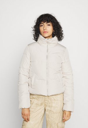  Lichtbeige pufferjack met een hoge kraag, een rits aan de voorkant en twee zijzakken. Zachte textuur met gequiltte secties voor isolatie.