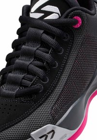 Zapatilla deportiva negra con material de malla y sintético, con cordones negros, detalles en rosa, lados texturizados y una suela estampada.