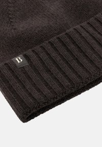 Mustardaga kootud beanie, millel on tekstuuriga ribidega äär. Ees on väike ristkülikukujuline silt, millel on valge täht "B". Pehme materjal.