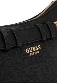 Borsa a tracolla nera in finta pelle con superficie testurizzata, accento del logo in tono oro e chiusura con zip. Presenta dettagli decorativi sulle cinghie.