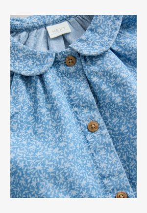 Cămașă cu imprimeu floral albastru, cu guler rotund, închidere cu nasturi și material texturat. Nasturii sunt de culoare lemn deschis, cu un design circular.