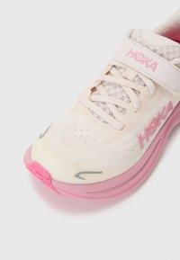 Chaussure de running légère avec une tige en maille crème, des accents roses, une semelle rembourrée et une sangle sécurisée au niveau du métatarse.