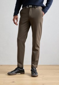Brune skreddersydde bukser med en glatt tekstur, med sidelommer og et svart belte med hvite striper. Brukt med svarte sneakers.
