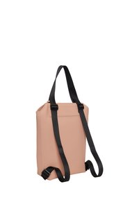 Vaaleanpunainen synteettisestä nahasta valmistettu reppu, jossa on mustat säädettävät hihnat, varustettu vetoketjukiinnityksellä ja suorakulmaisella muodolla. Minimalistiseen muotoiluun keskittyvät yksityiskohdat.