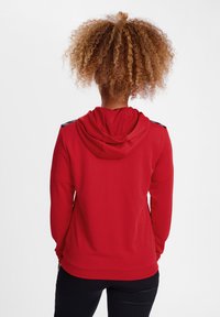 Rote Kapuzenjacke mit Kordelzug, strukturierter Stoff und schwarzen Akzenten an den Schultern. Figurbetonter Schnitt mit geripptem Saum und Bündchen.