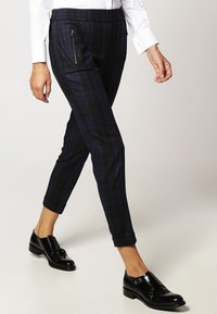 Spodnie w granatową kratę o slim fit, z elastycznym pasem i bocznymi kieszeniami na zamek; zestawione z błyszczącymi czarnymi skórzanymi butami.