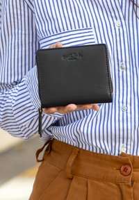 Juodas odinis piniginė su užtrauktuku, su iškilmingu logotipu, stačiakampio formos, lygaus paviršiaus ir mažo užtrauktuko traukimo.