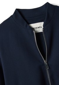 Marineblaue Jacke zum Reißverschluss mit hohem Kragen, weichem Stoff, metallischem Reißverschluss und sichtbarem Markenschild im Kragenbereich.