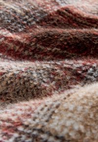 Textil de lana en tonos marrones y rojos, con un patrón de cuadros. La superficie parece suave con una textura ligeramente borrosa.