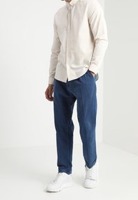 Beige overhemden met een spread collar, gecombineerd met marineblauwe broeken en witte sneakers, die een relaxte pasvorm en een soepele stof uitstralen.