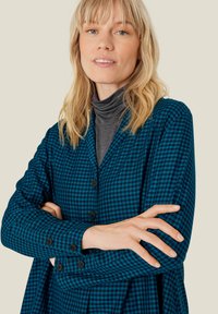 Niebieska i czarna koszula w kratę z długim rękawem, z przodem zapinanym na guziki i luźnym krojem. Posiada miękką fakturę oraz zaokrąglony kołnierz.