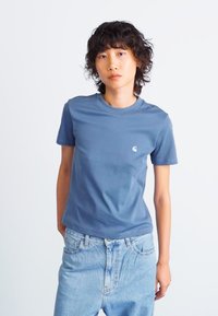 Blå bomulls T-skjorte med rund hals og korte ermer, med en liten logo på venstre bryst. Sammen med lyseblå denimjeans.