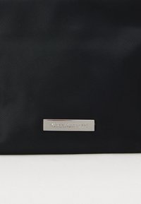 Μαύρη νάιλον τσάντα με ασημένια ορθογώνια πλακέτα λογότυπου ανάγλυφα με τη γραφή "KARL LAGERFELD." Λείος υφασμάς, απλός σχεδιασμός και καθαρές άκρες.