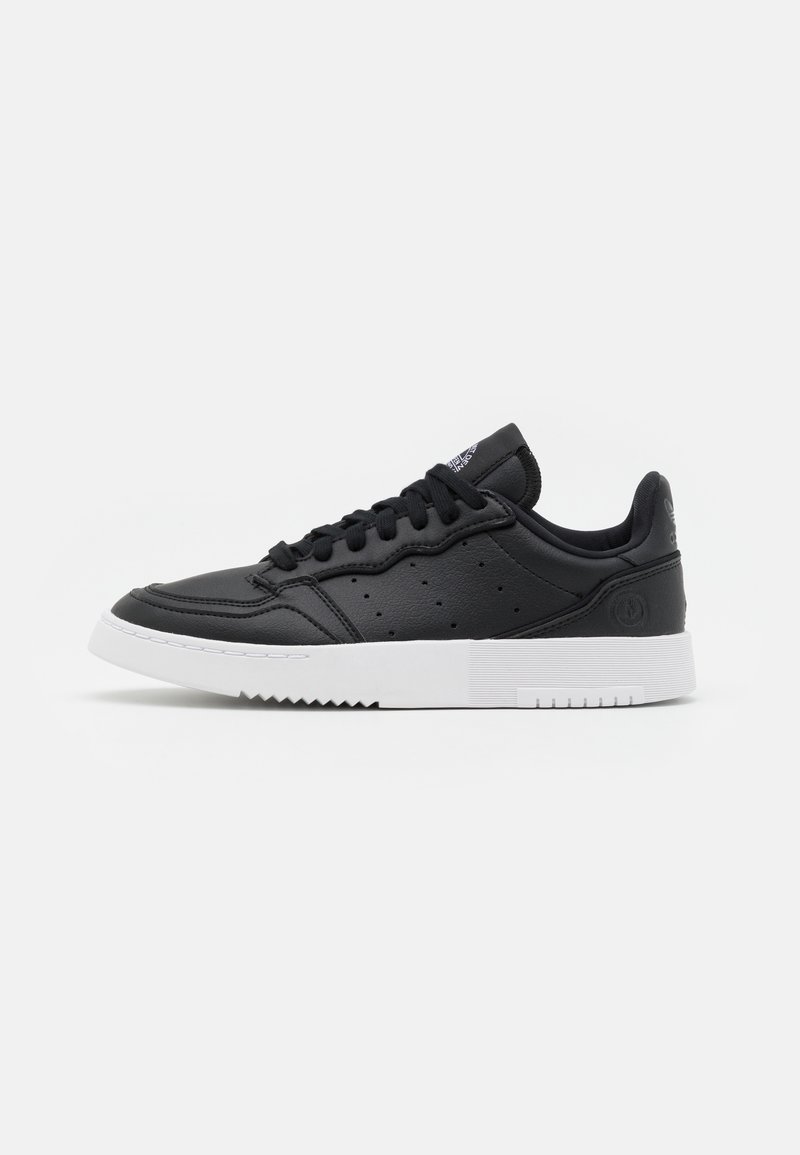 Black low-top sneaker with lace-up front, perforated side panels, and thick white textured sole on a white background.