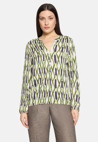 Bluzka z długim rękawem w zielono-białym kolorze, ozdobiona wzorem diamentowym z fioletowymi akcentami, z dekoltem w kształcie litery V i listwą z guzikami. Lekka tkanina.