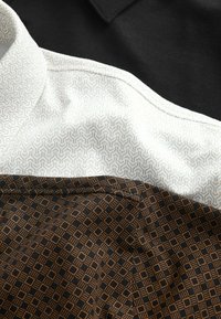 Gros plan de sections de tissu : noir uni, blanc avec un motif géométrique clair et marron avec un motif en grille losange foncé.