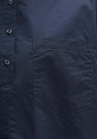 Camisa de botonadura en azul marino, confeccionada en tejido suave, con un bolsillo en el pecho y costuras en contraste, además de un cuello estructurado.