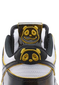 Svart och vit sneaker med gul panda broderi på hälfliken, glansigt material, vadderad krage och kontrasterande sömnadsdetaljer.