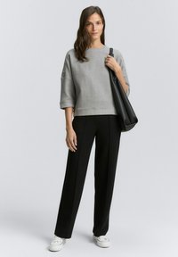 Grauer, kurzer Sweatshirt mit strukturiertem Stoff und weiten Ärmeln, kombiniert mit schwarzen Straight-Leg-Hosen und weißen Sneakern. Schwarze Handtasche als Accessoire.