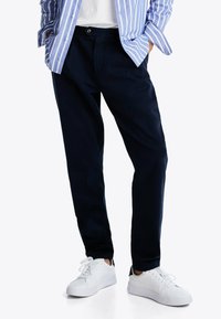 Pantalones de algodón azul marino con un corte relajado, bolsillos frontales y un cierre de un solo botón, combinados con zapatillas blancas y una camisa a rayas azul.