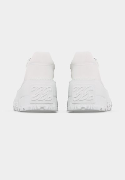 Paire de baskets blanches épaisses vues de dos, avec des semelles texturées épaisses ornées de motifs de vagues embossés.