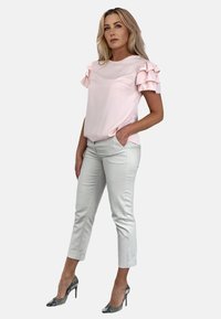 Jasnoróżowa bluzka z falbaniastymi krótkimi rękawami, w zestawieniu z jasnobeżowymi spodniami 7/8 i srebrnymi szpilkami w szpic. Gładki materiał, dopasowany krój.