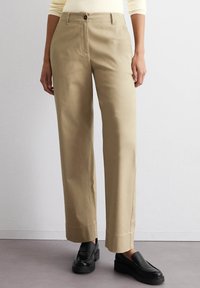 Beige wijde broek met knoopsluiting aan de voorkant, voorzakken en omgeslagen zoom. Structuur katoen, gecombineerd met zwarte instappers.