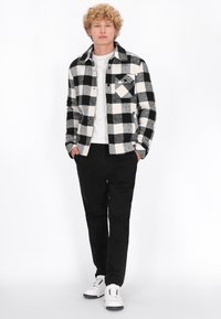 Mustvalge ruuduline flanellipeace, millel on krae ja esikoted; koos mustade püksidega ja valgete tossudega. Sile kangastekstuuri.