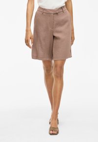 Pantaloni corti marroni fino al ginocchio con un tessuto texturizzato e una vestibilità rilassata. Presentano una vita con passanti per cintura e tasche laterali.
