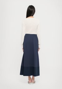 Maxi-Rock in Marineblau mit tailliertem Bund und fließendem Design. Weicher Stoff mit einem dunkleren Saum, kombiniert mit einem hellen Langarmtop.