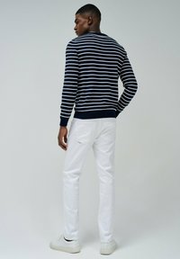 Maglione a righe marine e bianche con maniche lunghe, polsini e orlo a coste. Abbinato a pantaloni bianchi, con una linea elegante e dettagli minimi.