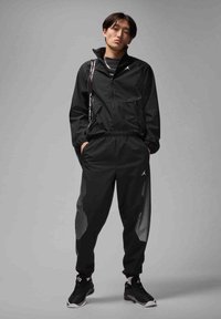 Black athletic tracksuit with a zippered jacket and elastic waistband pants, featuring dotted pattern details and Jordan logo accents.