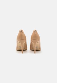 Nude high-heeled shoes with a smooth leather finish, pointed toe, and silver logo accent at the back, featuring a slender stiletto heel.
