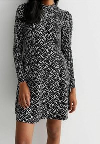 Svart långärmad klänning med vita prickar, åtsittande liv, något utställd kjol och hög halsringning. Slät, elastisk tyg.