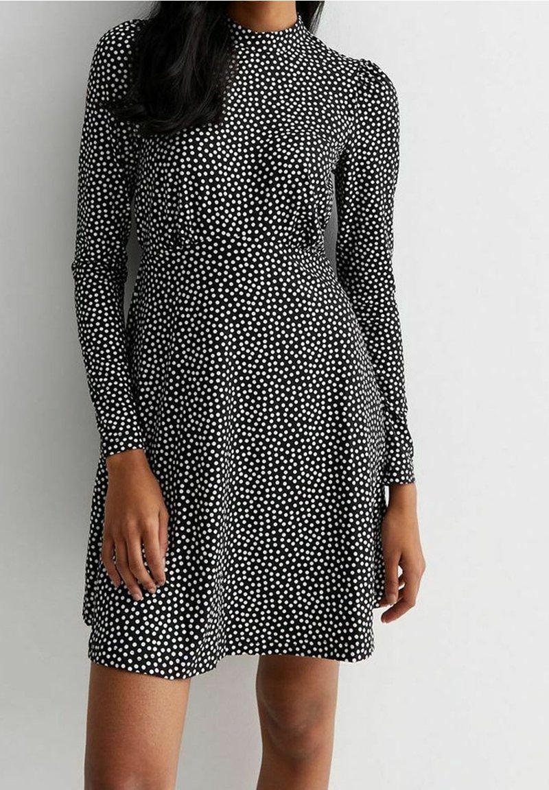 Svart långärmad klänning med vita prickar, åtsittande liv, något utställd kjol och hög halsringning. Slät, elastisk tyg.