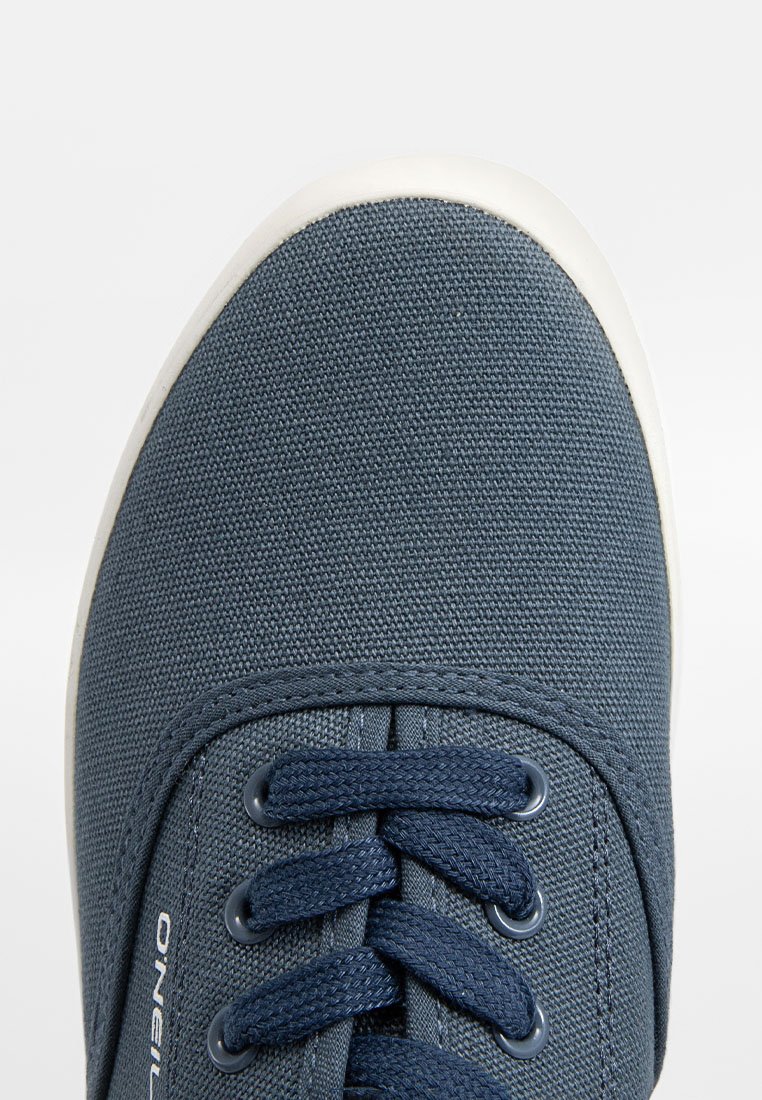 Zapatilla de lona azul marino con puntera redondeada, parte delantera con cordones, suela de goma blanca y detalles de tela texturizada. Logotipo de la marca visible en el lateral.