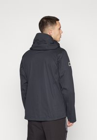Veste noire imperméable avec col haut, coutures visibles et manches longues. Présente un logo sur le bras supérieur et une coupe légèrement ample.