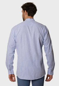 Camisa de manga larga azul claro con una tela texturizada, diseño sin cuello y puños con botones. Dobladillo recto con sutiles rayas verticales.