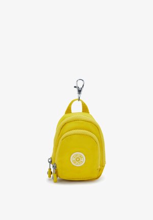Pieni keltainen kangasminireppu avaimenperässä, jossa on etutasku, vetoketjut ja metallinen klipsi kiinnitystä varten.