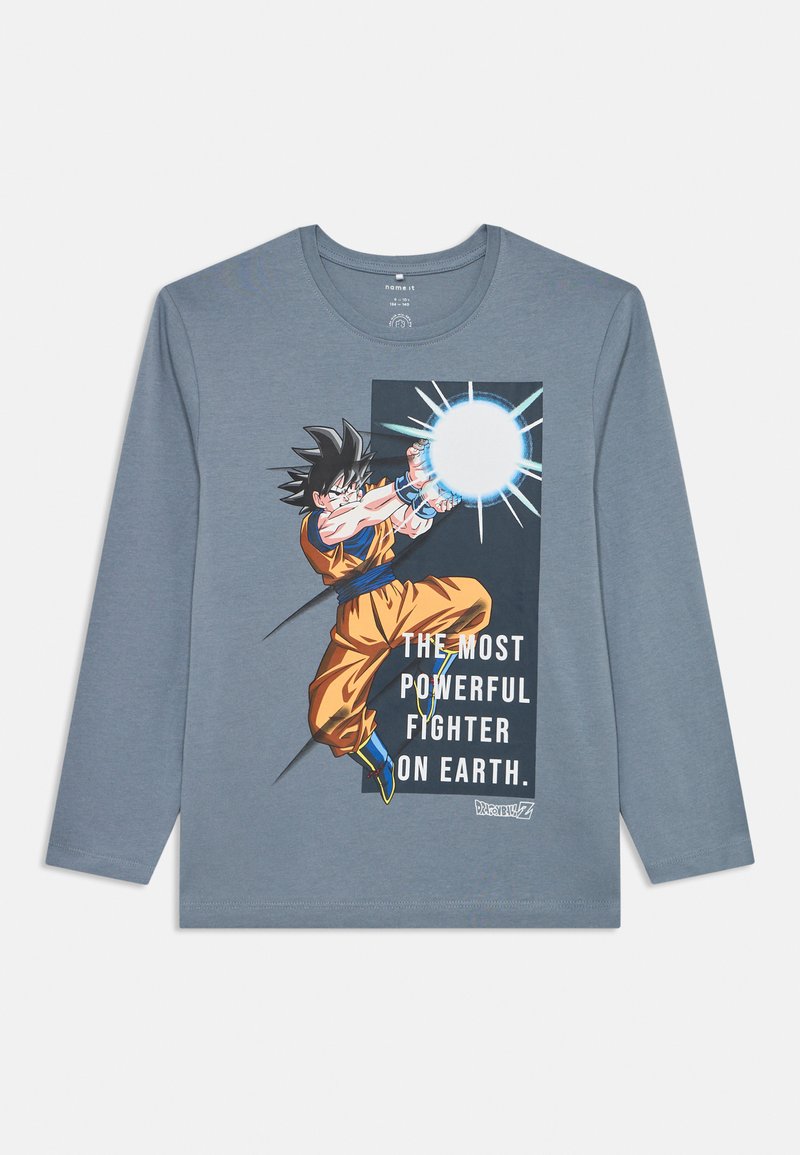 Hosszú ujjú szürke póló, színes grafika egy karakterről, aki narancssárga öltözetet visel, felirattal: "A LEGHATALMASABB HARCOS A FÖLDÖN."